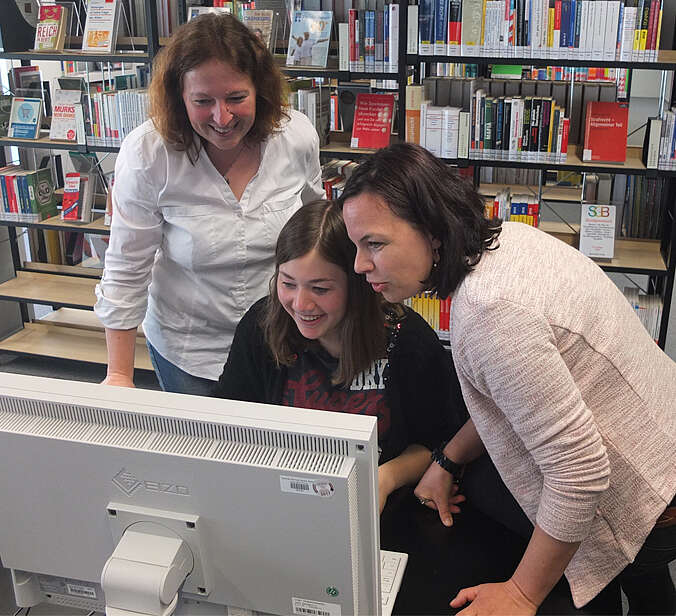 Zwei Frauen helfen einem Kind am Computer