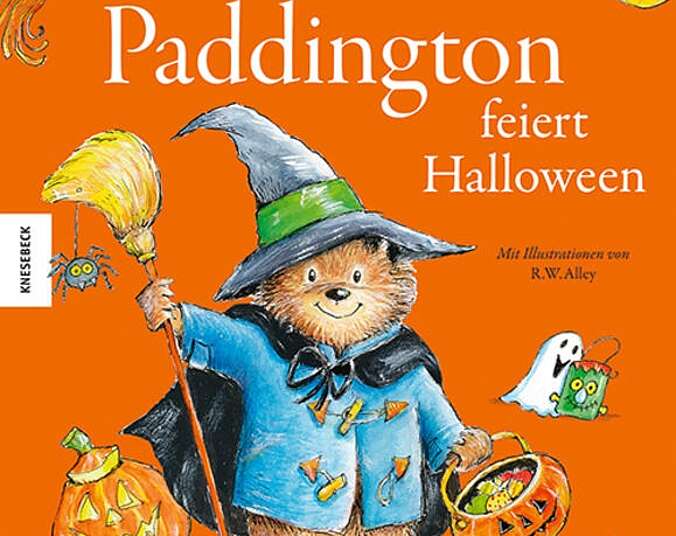Paddinton mit Hexenhut, Umhang, Besen und einem Kürbis voller Süßigkeiten.